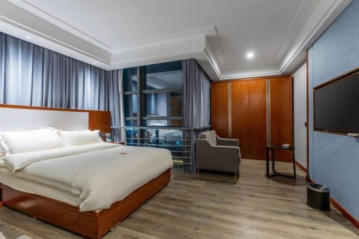 Habitación de hotel con cama, televisor, zona de estar y vista a la ciudad.
