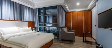 A hotel room with a bed, a TV, a seating area, and a view of the city.