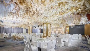 Un salón de banquetes con mesas redondas, sillas blancas y un techo decorado con motivos florales.