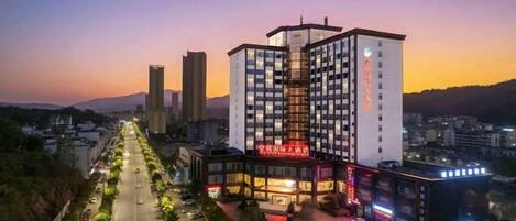 A multi-story hotel with a prominent entrance, a parking area, and a view of the surrounding cityscape.