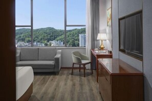 Een hotelkamer met een bank, fauteuil, bureau, lamp en een televisie.