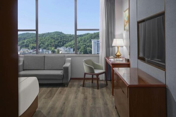 Habitación de hotel con sofá, sillón, escritorio, lámpara y televisor.