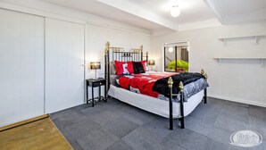 Een slaapkamer met een bed, nachtkastjes, een garderobe en een raam met uitzicht op groen.