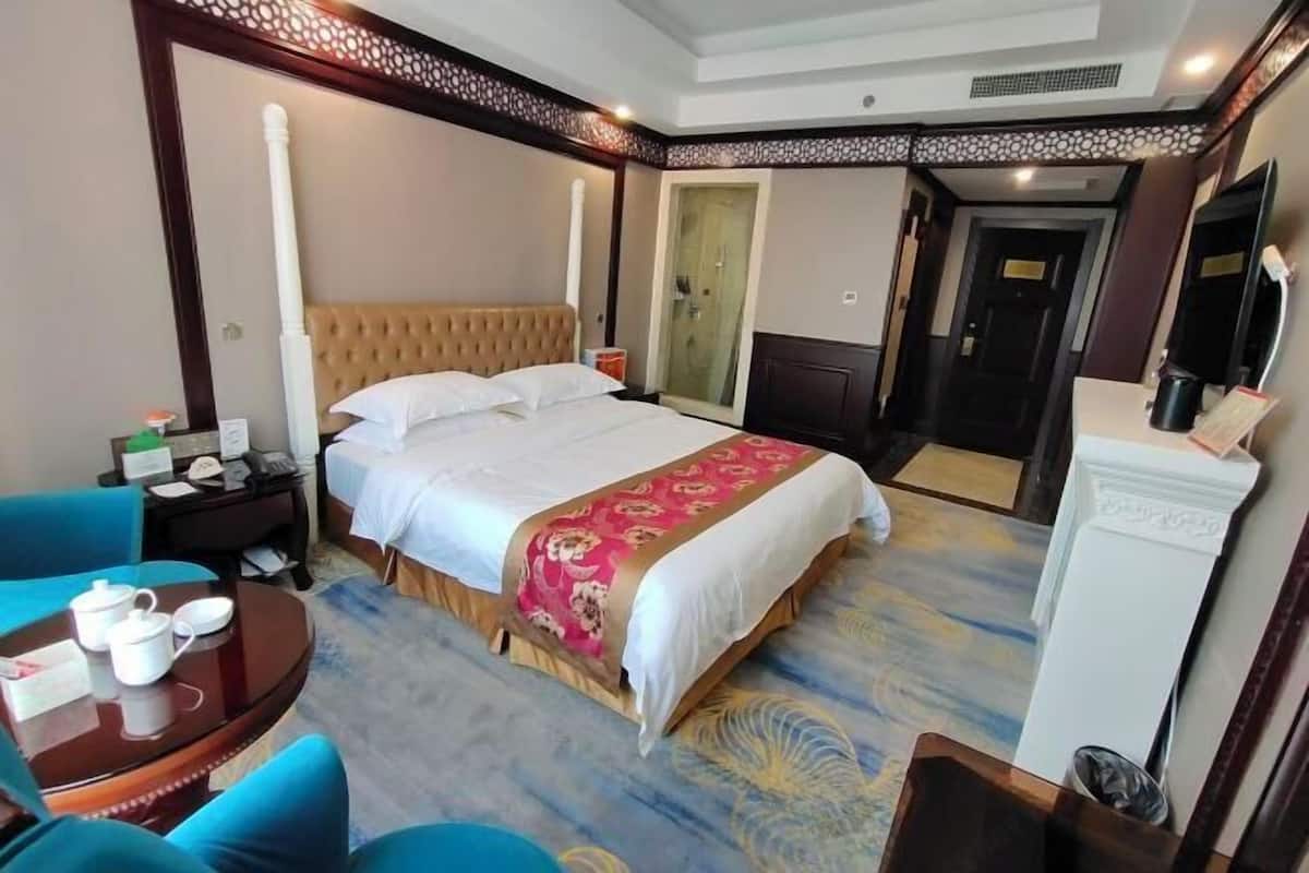 A hotel room with a large bed, a round table with a teapot, and a chair.