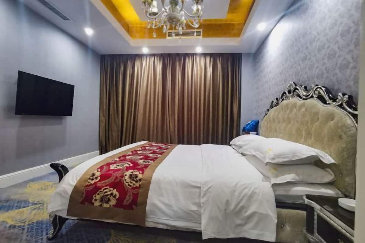 A hotel room with a bed, curtains, a television, and a chandelier.