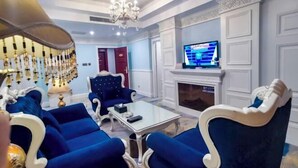 Una sala de estar con muebles tapizados en azul, una mesa de centro de vidrio, una araña, una chimenea y un televisor.