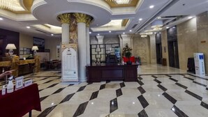 Un vestíbulo de hotel con una recepción, mostradores de registro y un candelabro.