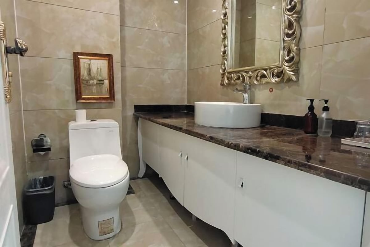Un baño con inodoro, lavabo, tocador, espejo y un cuadro en la pared.