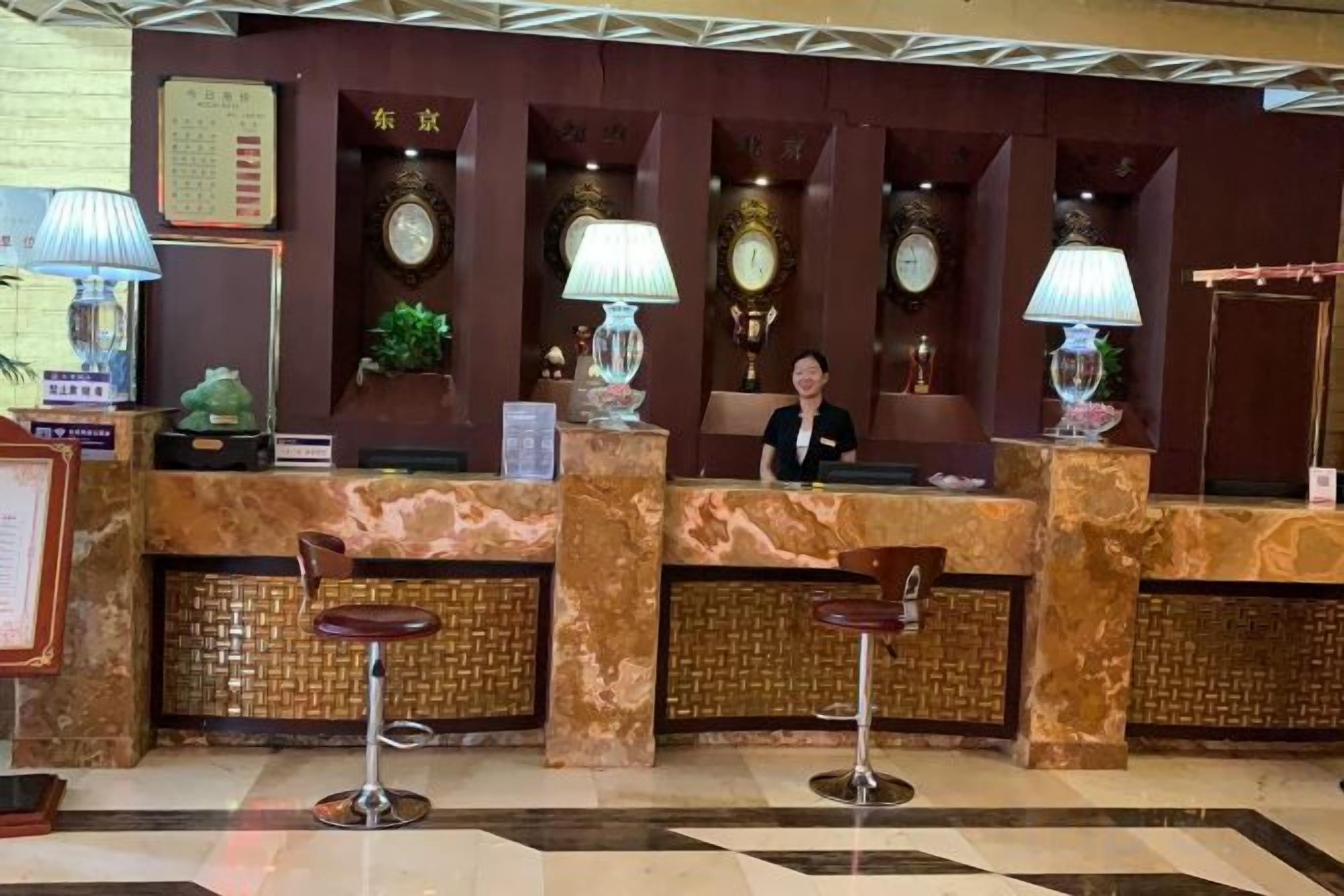 A hotel reception area with a marble counter, two bar stools, and a receptionist.