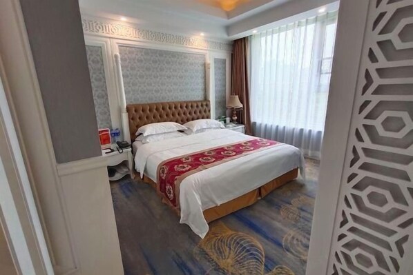 Une chambre d’hôtel avec un grand lit, une table de chevet, une lampe et une fenêtre avec des rideaux.