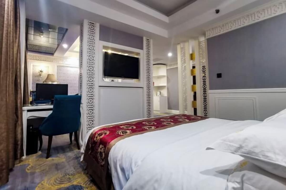 Habitación de hotel con cama, escritorio con computadora, televisor montado en la pared y paneles decorativos.