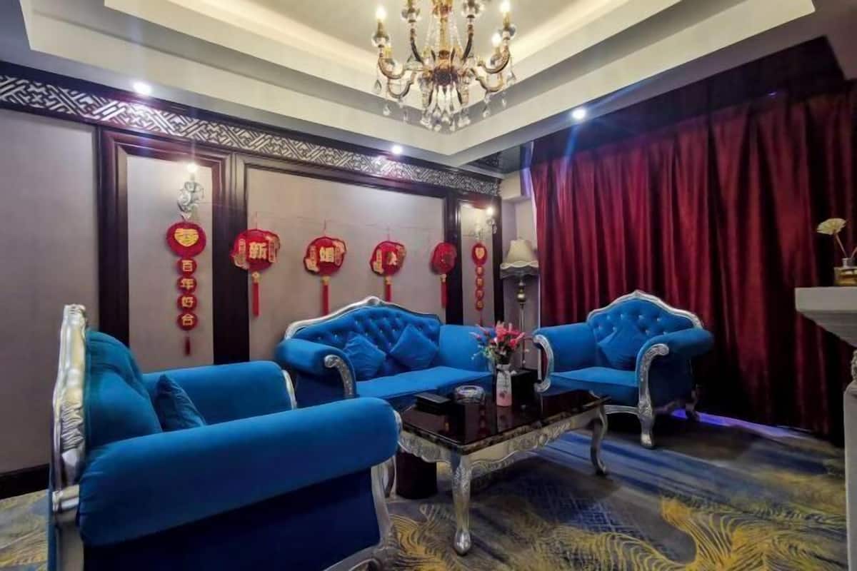A room with a blue sofa set, a chandelier, and red decorations on the wall.