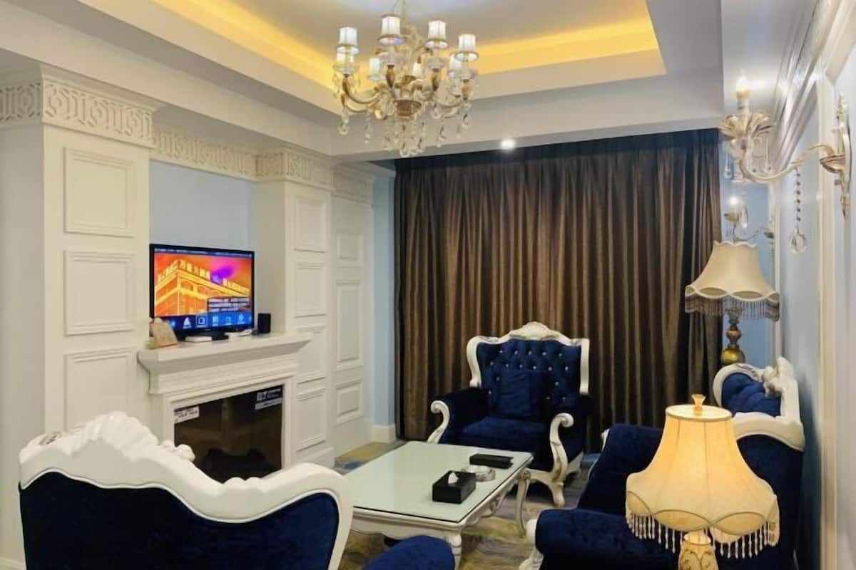 A living room with a television, a fireplace, a chandelier, and blue upholstered furniture.