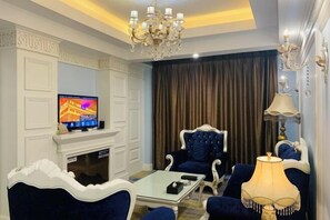 Una sala de estar con televisor, chimenea, candelabro y mobiliario tapizado en azul.
