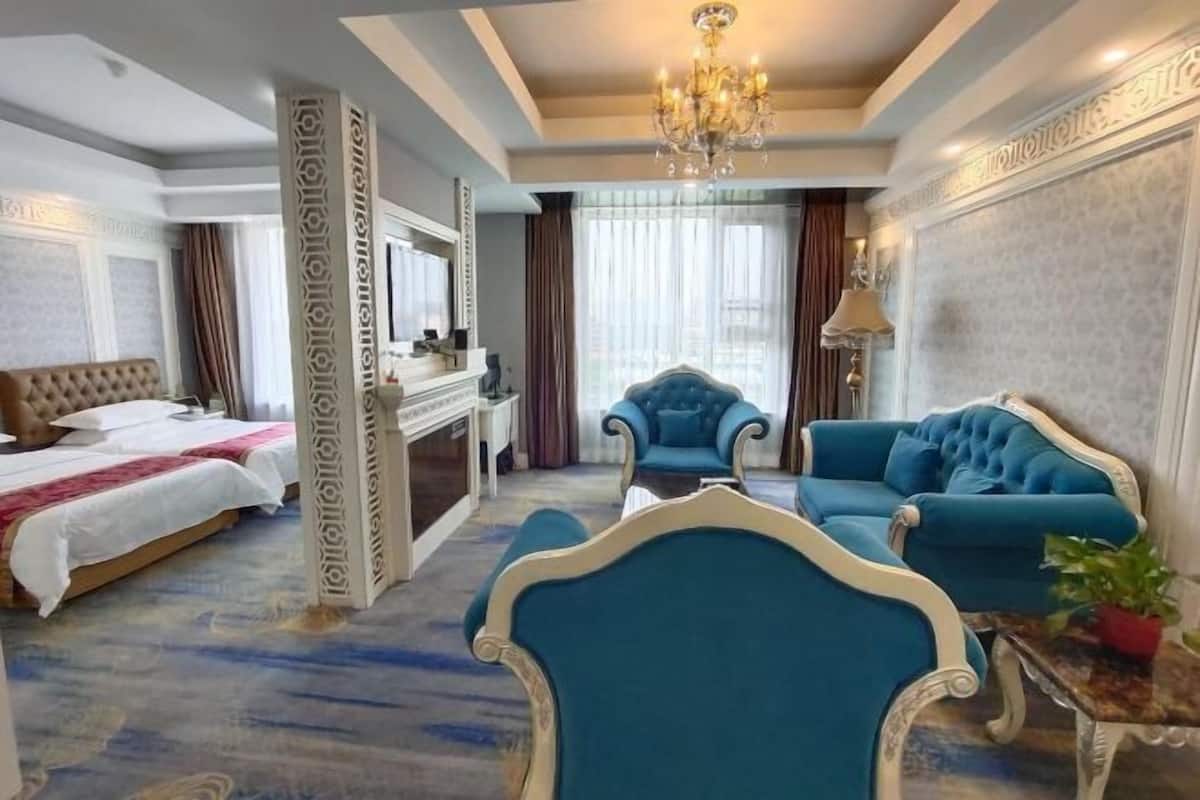 A hotel room with a bed, two armchairs, a sofa, a chandelier, and a large window with curtains.