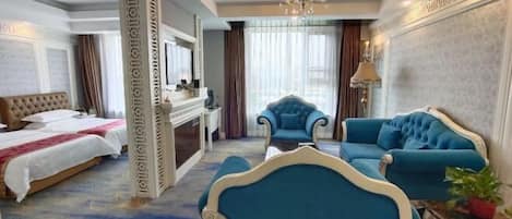 A hotel room with a bed, two armchairs, a sofa, a chandelier, and a large window with curtains.