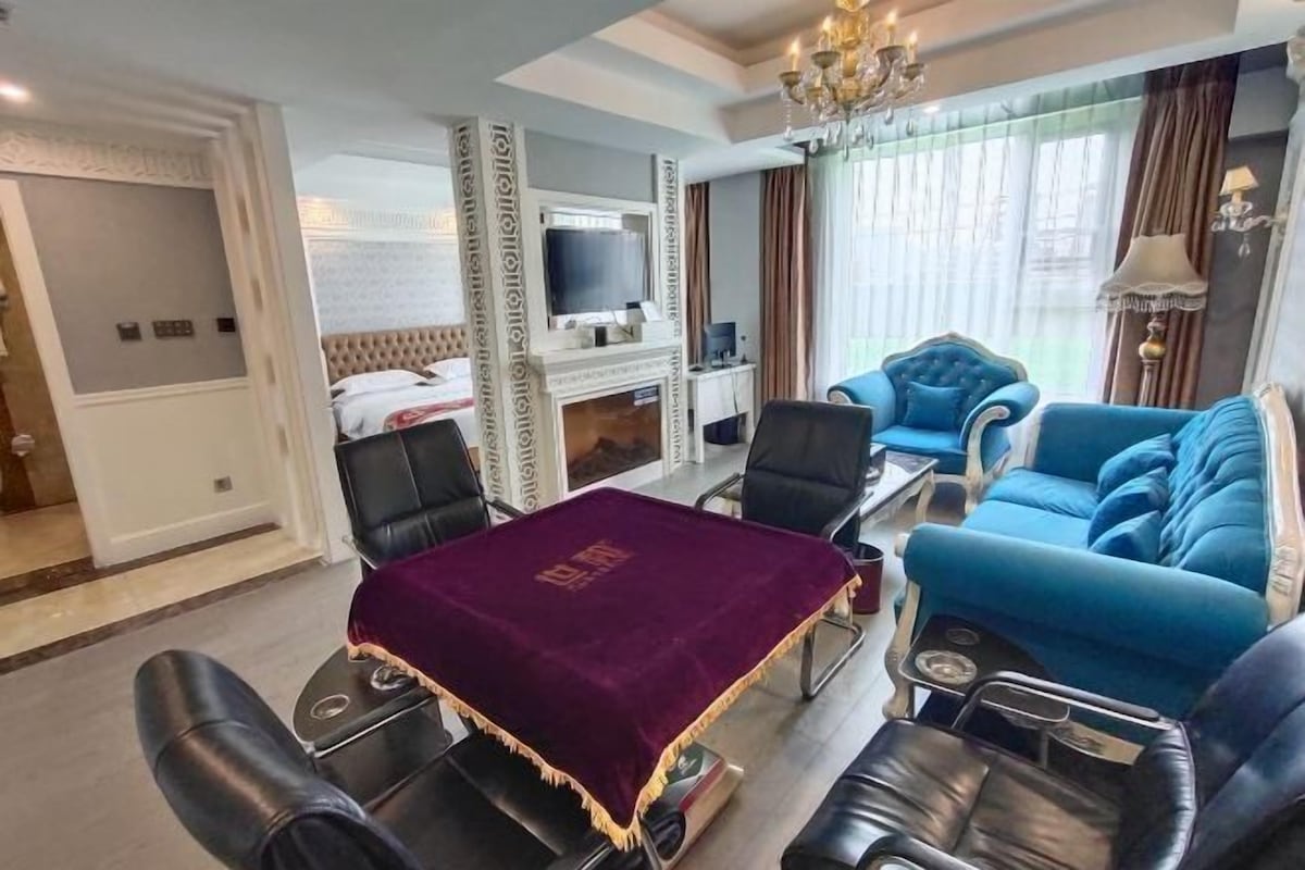 Una habitación de hotel con cama, televisor, sofá, mesa de comedor con sillas y un candelabro.