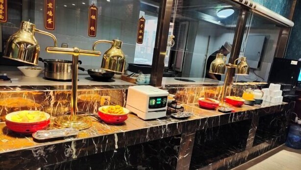 Un mostrador de buffet con diversos platos, una cafetera y un reloj digital.
