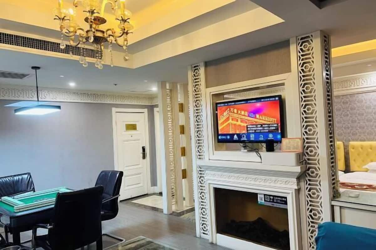 A hotel room with a fireplace, a television mounted above it, a dining area with a table and chairs, and a bed with a headboard.