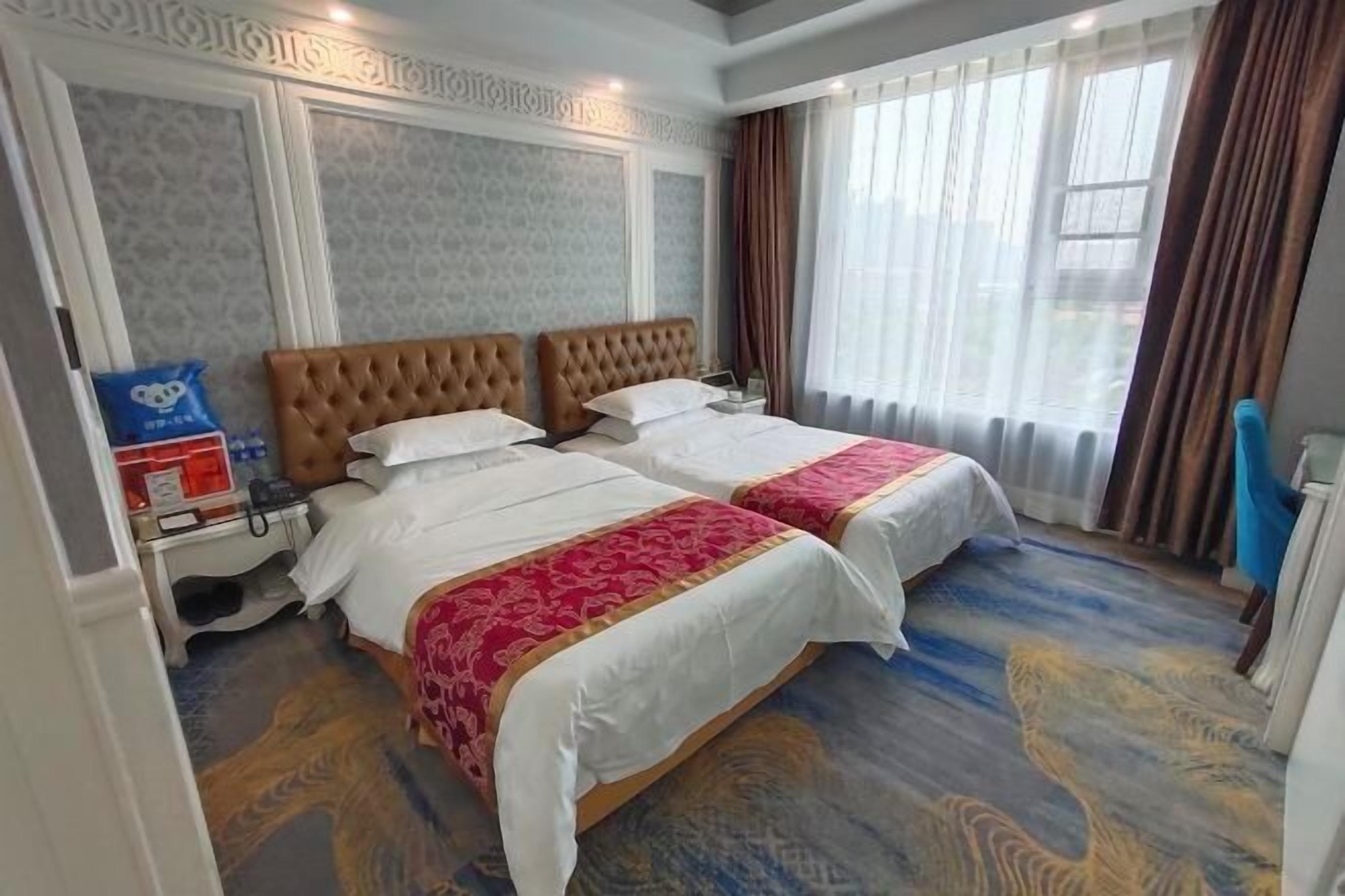 Une chambre d’hôtel avec deux lits, une table de chevet, un téléphone et une fenêtre avec des rideaux.