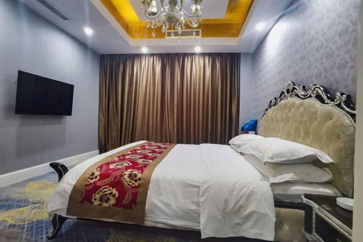 Una habitación de hotel con cama, televisión montada en la pared y un candelabro.