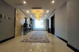 Corredor de hotel com piso de mármore, tapete estampado e um candelabro.