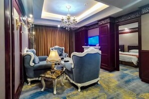 Habitación de hotel con candelabro, un sillón azul, una mesita con lámpara y una cama con cabecera azul.