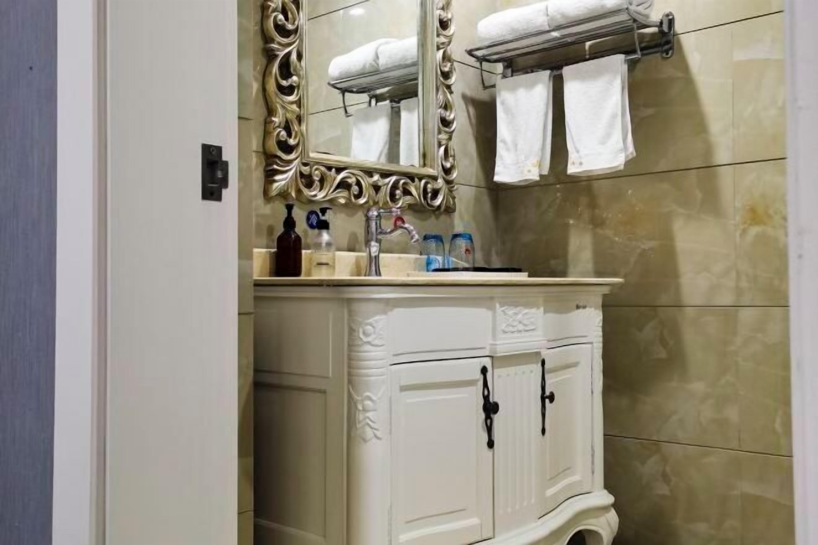 A bathroom with a white vanity, a mirror with an ornate frame, and a towel rack with white towels.