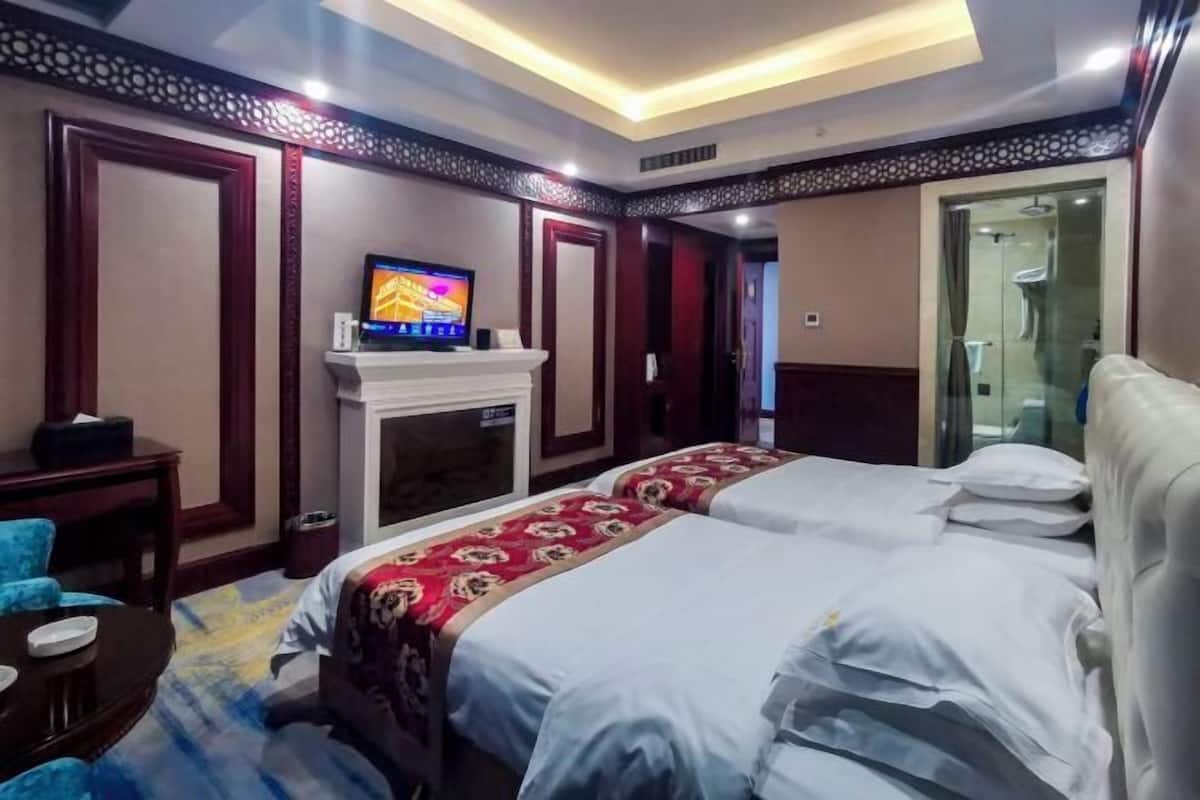 A hotel room with two beds, a television, a fireplace, and a glass shower.