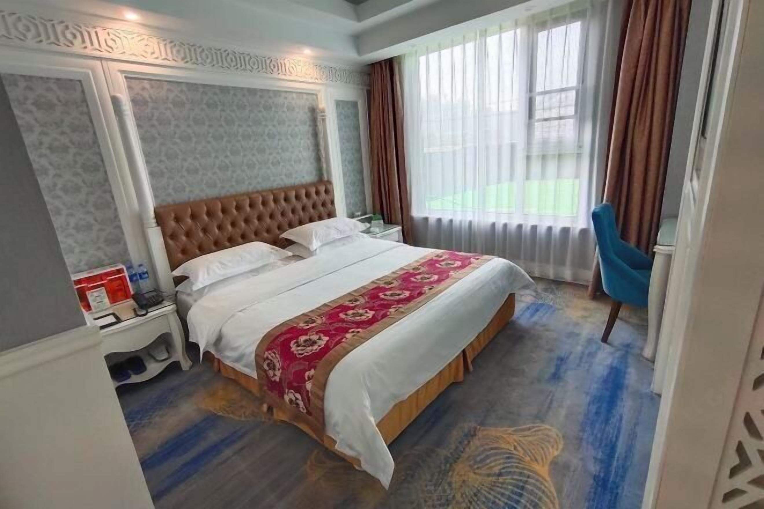 A hotel room with a large bed, a nightstand, a chair, and a window with curtains.