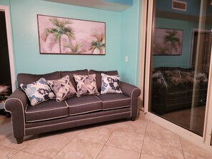Un salon avec un canapé marron foncé, quatre coussins à motifs, un mur de couleur turquoise et une grande fenêtre donnant sur une autre pièce.