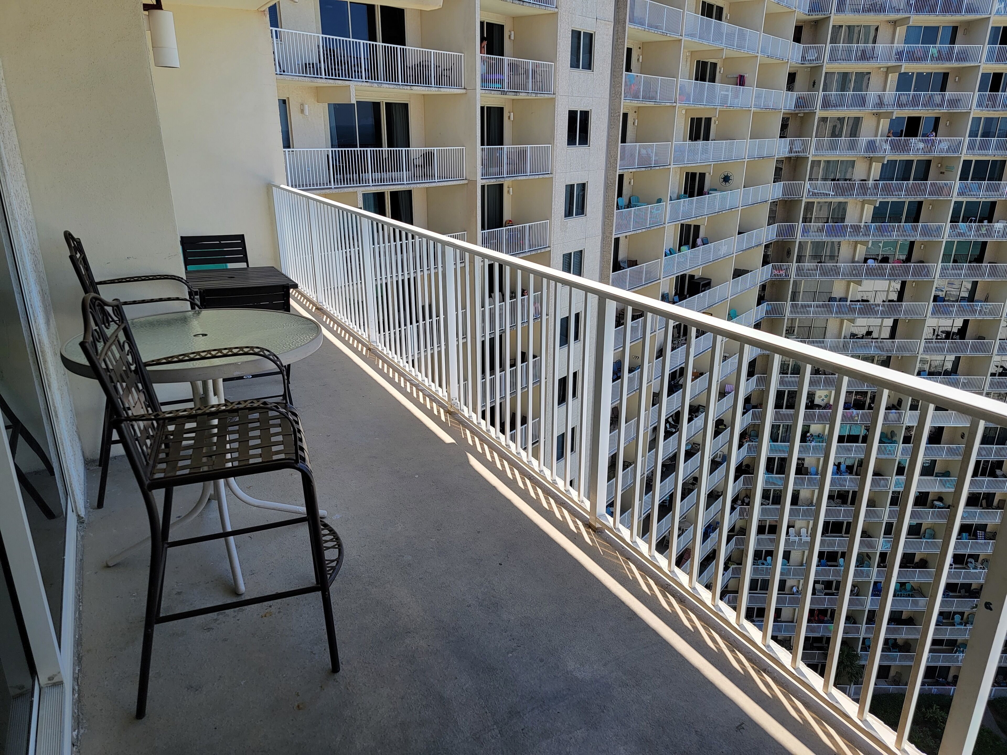 Un balcón con una mesa y sillas, con vistas a un edificio de varios pisos con balcones.