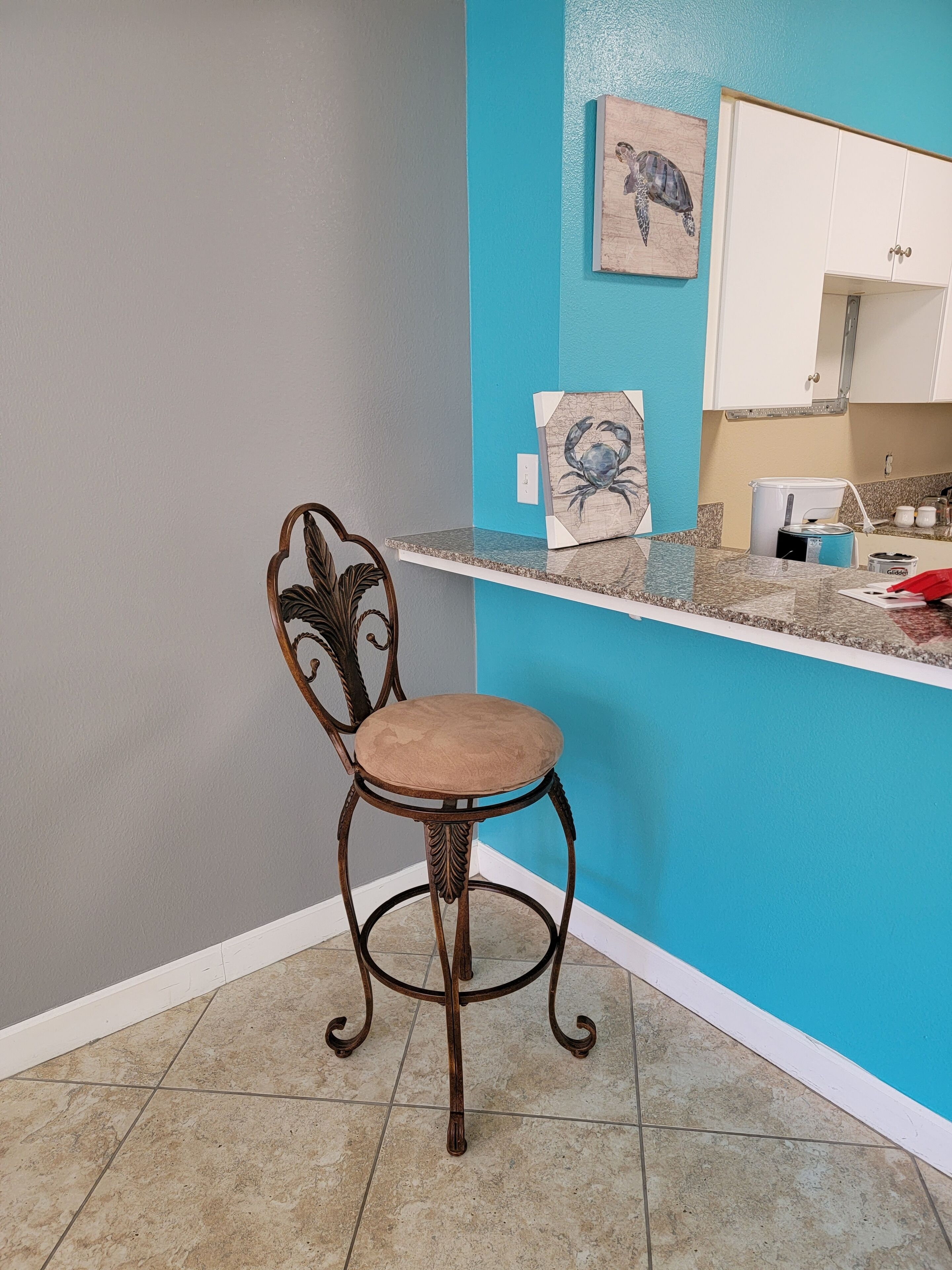 A chair with a cushioned seat and a decorative backrest in a room with a blue accent wall and a white cabinet.
