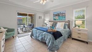 A bedroom with a bed, a nightstand, a chair, a window with blinds, and a door leading to a balcony. - Great for kids! Paddle boards, bikes, kayaks & pet friendly! Villa Evelyn's Palms - SWFL Rentals (Cape Coral)