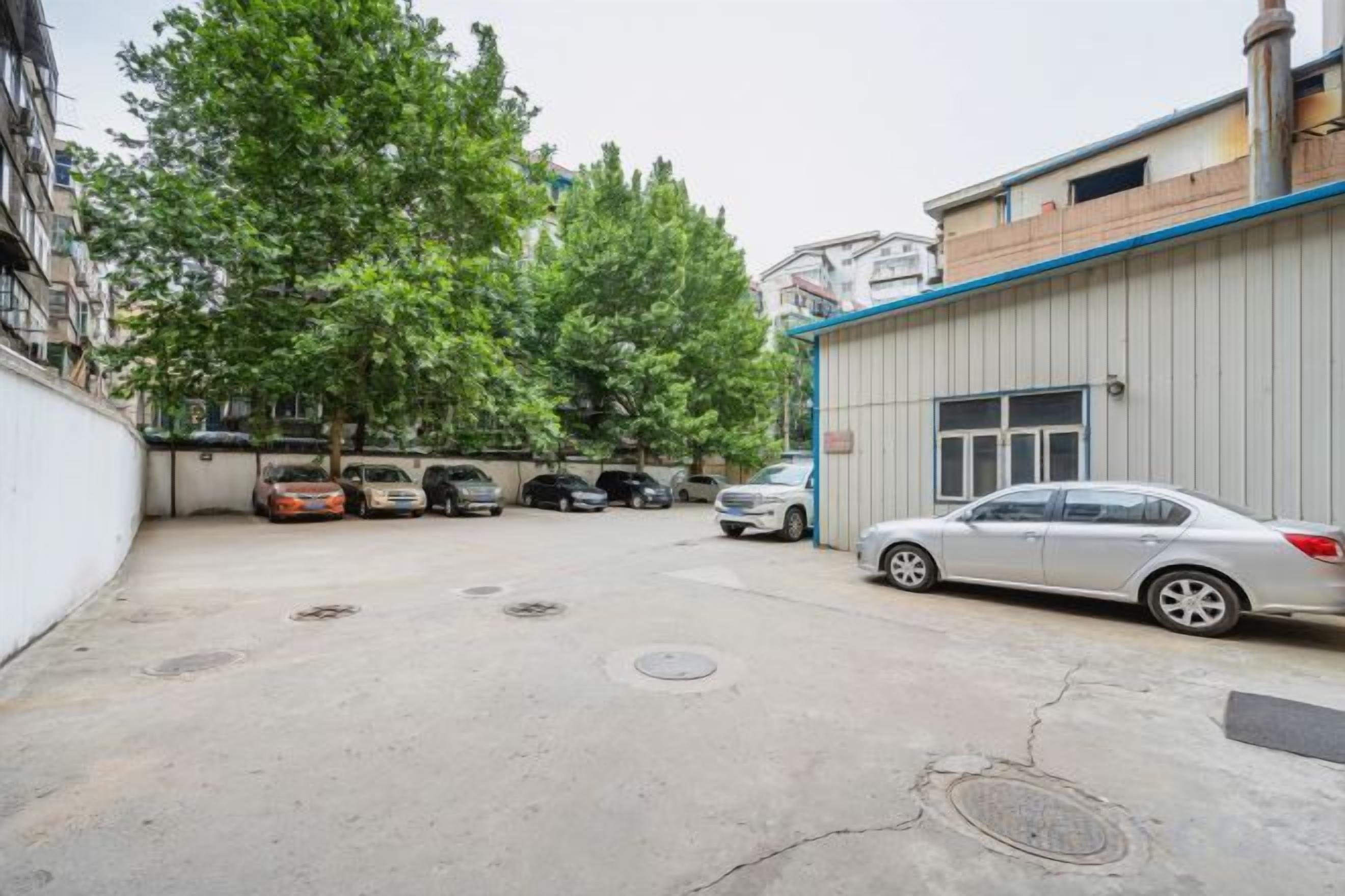 Uma área de estacionamento com vários carros, um edifício com detalhes em azul e árvores.