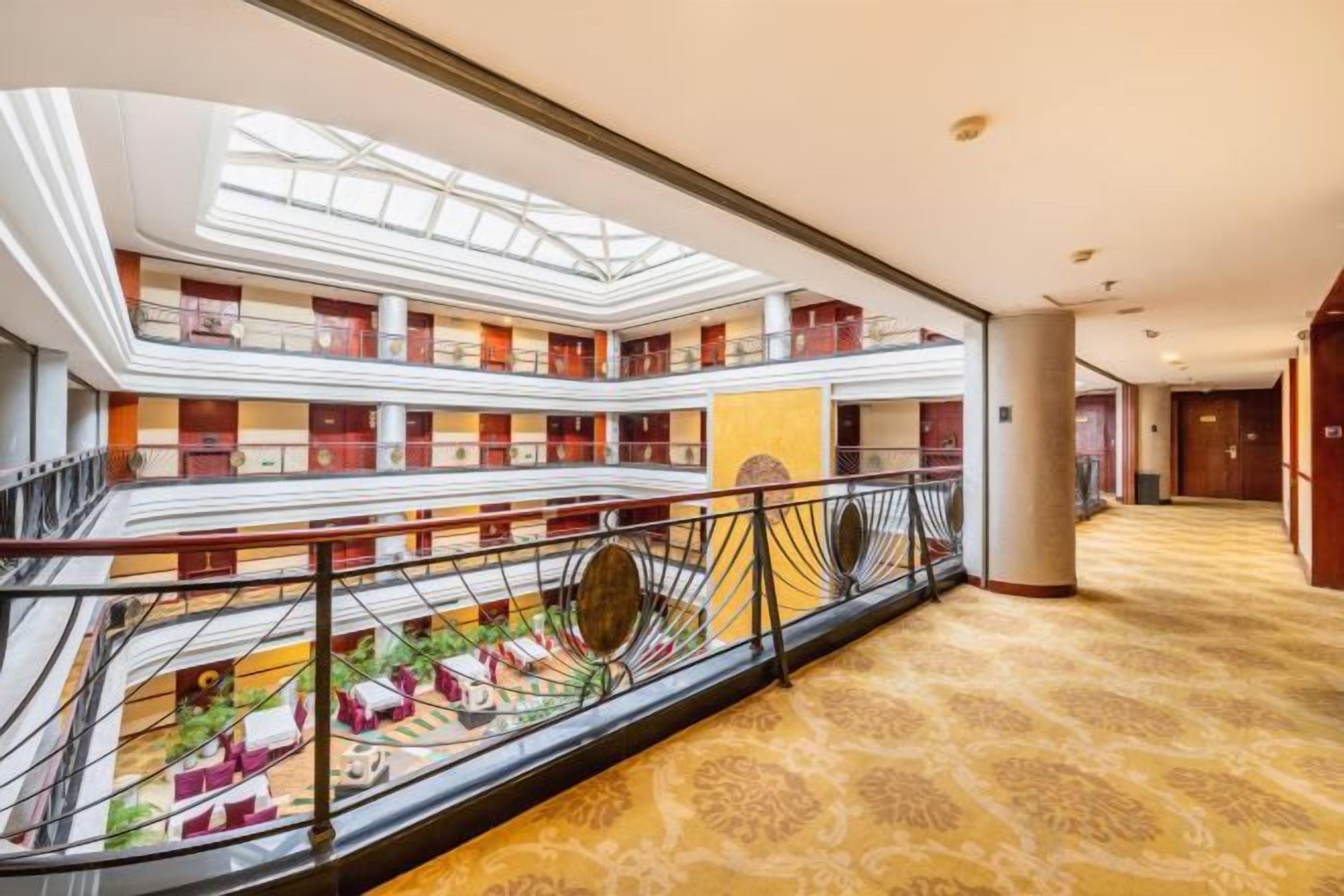Un vestíbulo de hotel de varios niveles con un patio central, balcones y una imponente escalera.