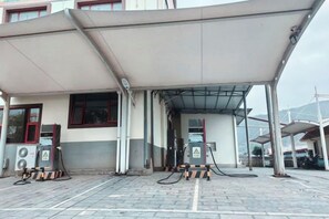 A covered fuel station with multiple pumps, a building in the background, and a paved ground.
