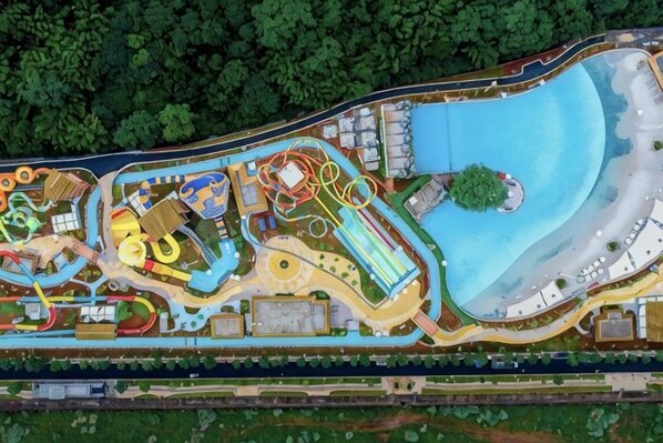 Vista aérea de un parque temático con diversas atracciones y espectáculos, una extensa masa de agua y una carretera circundante.