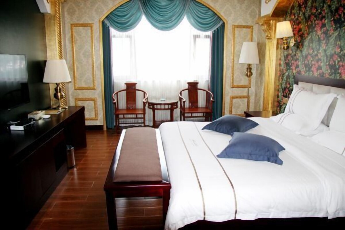 A hotel room with a large bed, a desk with a TV, two chairs, and a small table.