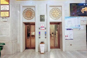 Um elevador com detalhes ornamentais, um visor digital e cartazes informativos nas paredes.