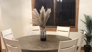 A round wooden dining table with white chairs, a vase with pampas grass, and a cowhide rug. - Your Montana Home Away From Home (Whitefish)