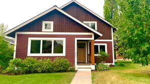 A two-story house with a front porch, a visible garage door, and a well-maintained lawn. - Your Montana Home Away From Home (Whitefish)