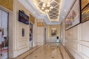 Ein Hotelkorridor mit einer Chandelier, gerahmten Kunstwerken und einem Empfangsbereich.