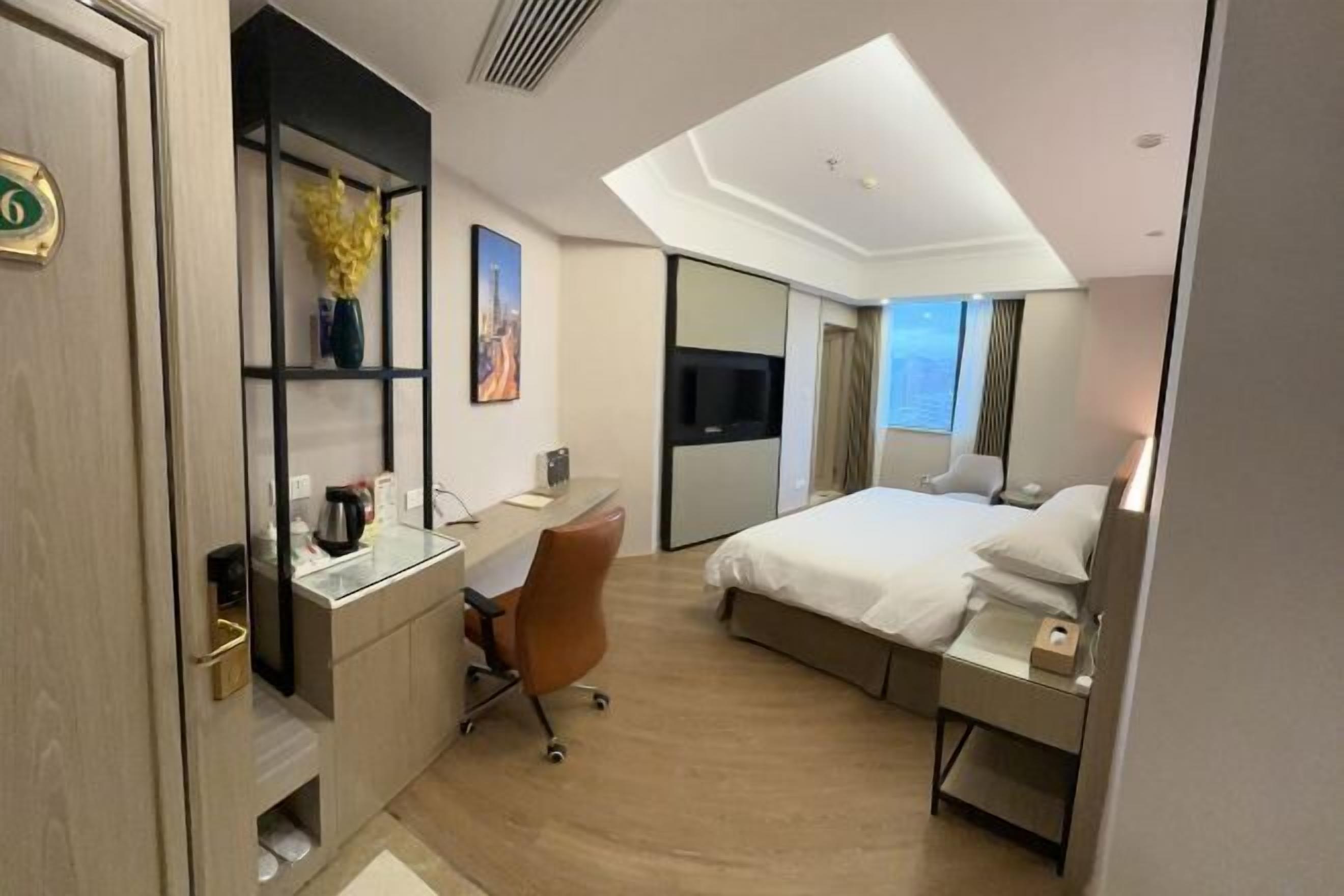 A modern hotel room with a desk, chair, bed, and a large mirror.