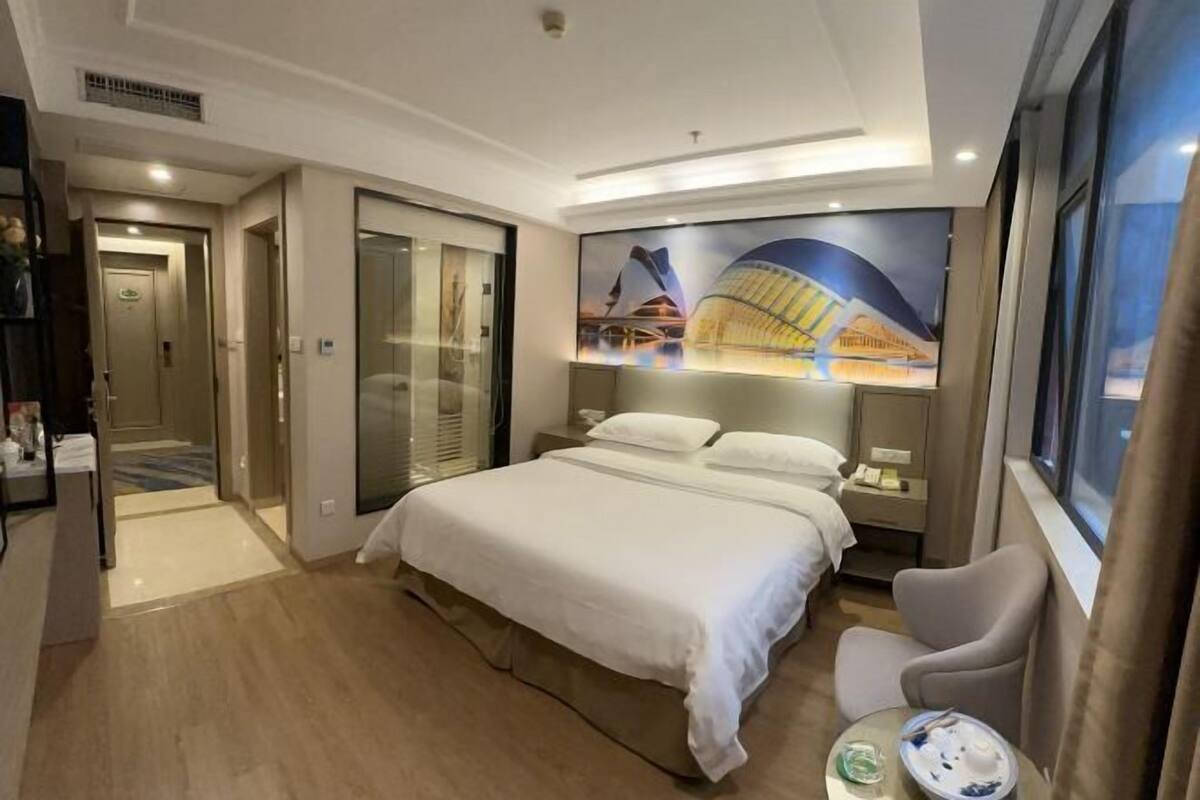 A hotel room with a large bed, a desk, a chair, a nightstand, and a window.