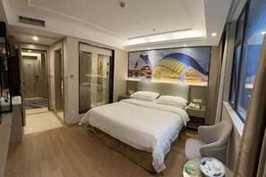 Una habitación de hotel con una cama grande, un escritorio, una silla, una mesita de noche y una ventana.