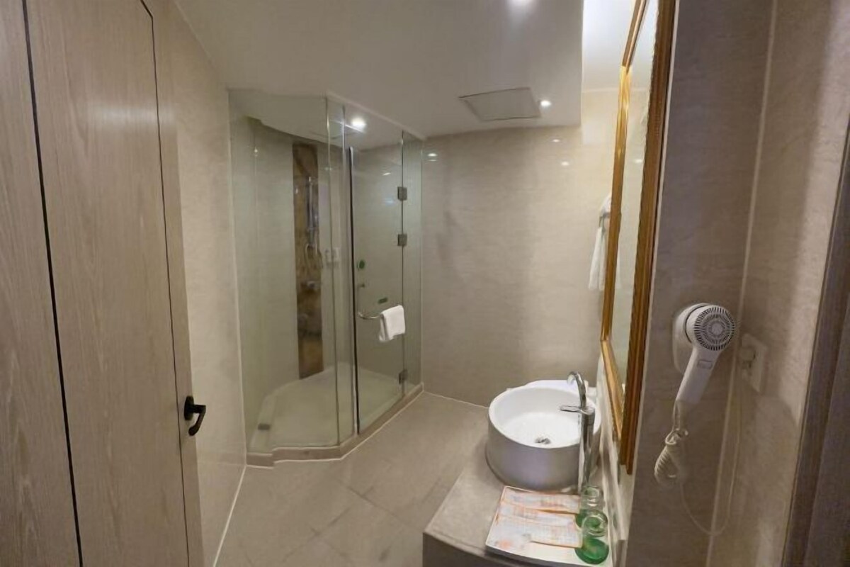 Ein modernes Badezimmer mit einer Duschkabine, einem runden Waschbecken und einem an der Wand montierten Fön.