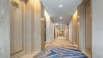 Pasillo de hotel con puertas de madera, alfombra estampada y un cartel que indica la dirección a la recepción.
