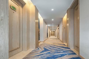 Pasillo de hotel con puertas de madera, alfombra estampada y un cartel que indica la dirección a la recepción.