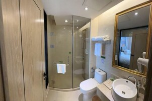 Un baño moderno con cabina de ducha de vidrio, inodoro, lavamanos y un espejo grande.
